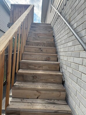 Eine Holztreppe mit Metallgeländern, die zu einem Gebäude mit Backsteinfassade führt.