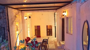 Un espacio al aire libre techado con mesa y sillas, una pared con ventana y un espejo.