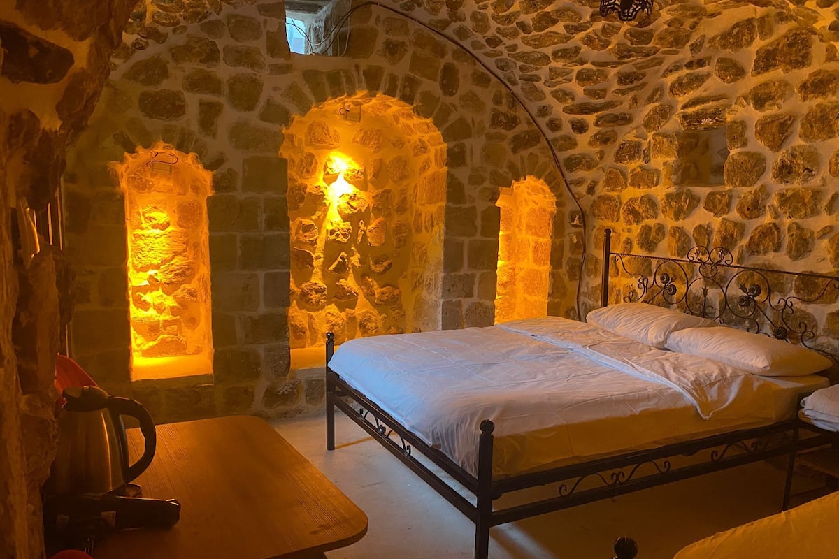 A stone-walled room with a bed, a table, and a bench.
