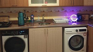 Una cocina compacta con armarios de madera, lavadora, secadora, cafetera y hervidor.
