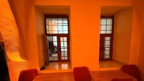 Un comedor con una mesa alta y seis sillas rojas, dos ventanas con cristales y una alfombra estampada en el suelo.