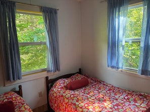 Una habitación con dos camas, una ventana con cortinas y vistas a zonas verdes.