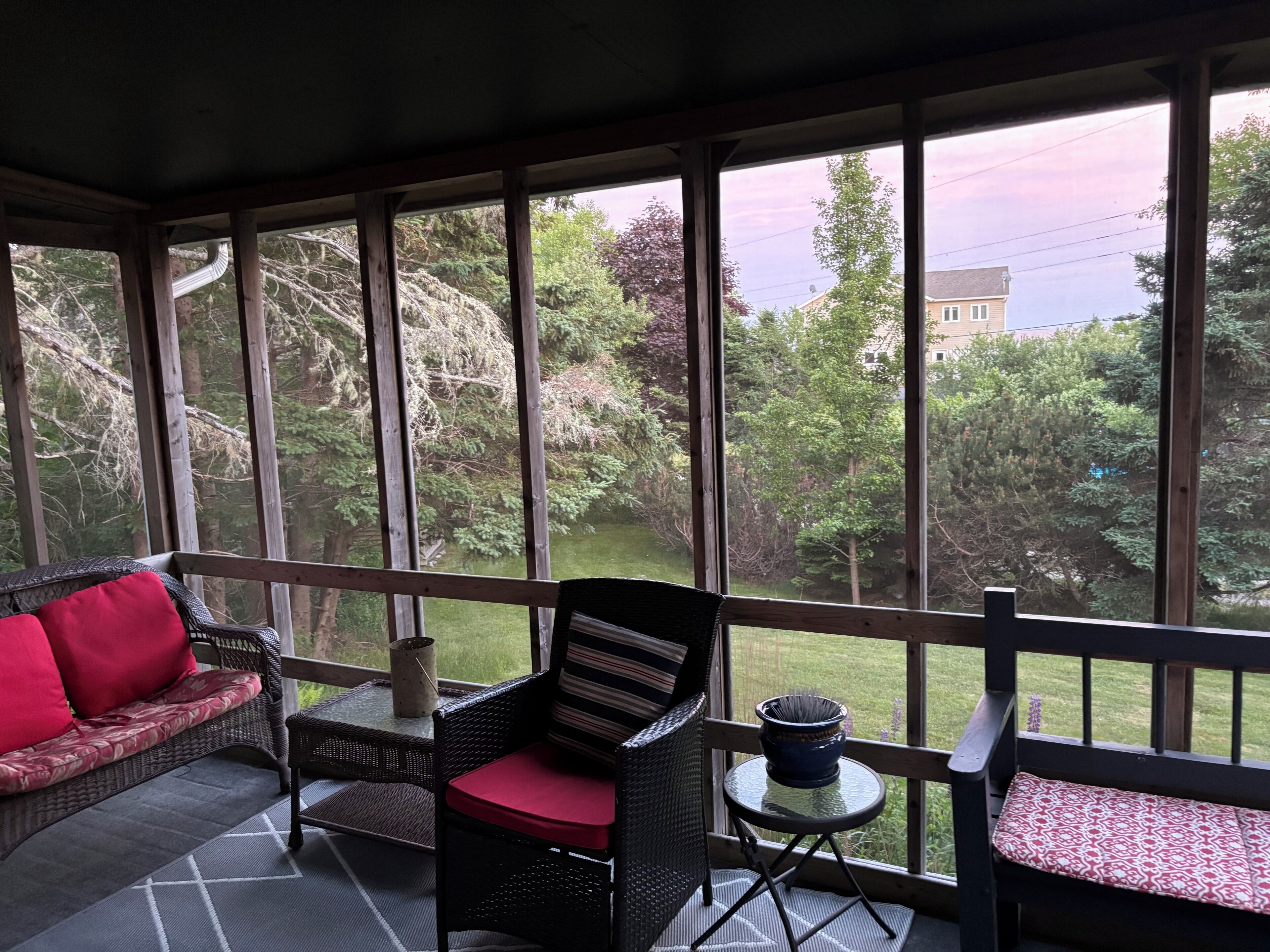 Une véranda aménagée avec des meubles en osier, une petite table et une vue sur un paysage verdoyant.