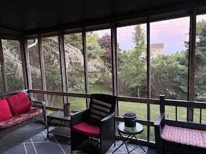 Une véranda aménagée avec des meubles en osier, une petite table et une vue sur un paysage verdoyant.