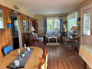 Une pièce chaleureuse avec une table à manger en bois, un ensemble de canapés, une carte accrochée au mur et une fenêtre avec des rideaux.