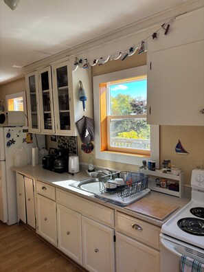 A kitchen with white cabinets, a window with a view, a sink, and a stove.