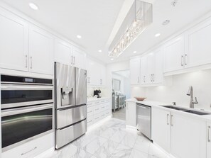 A modern kitchen with white cabinetry, stainless steel appliances, and a marble floor. - Luxury 3BR Townhome with Garden Oasis (Victoria)