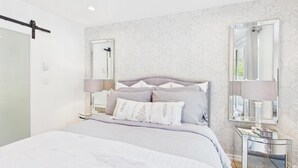 A modern bedroom with a large bed, bedside lamps, a glass side table, and a mirror. - Luxury 3BR Townhome with Garden Oasis (Victoria)