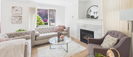 A modern living room with a fireplace, a sofa, a round coffee table, and a glass table with decorative items.