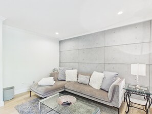A modern living room with a sectional sofa, a glass coffee table, and a side table with a lamp. - Luxury 3BR Townhome with Garden Oasis (Victoria)