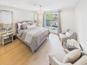 A modern bedroom with a large bed, bedside tables, a chair, and a view of the outdoors. - Luxury 3BR Townhome with Garden Oasis (Victoria)