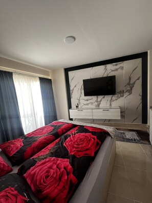 A bedroom with a bed, a TV mounted on the wall, and a window with curtains. - Hurghada Tiba Golden Resort Apartment Studio Room Ocean Beach Pool 21 (Al-Bahr al-ahmar)