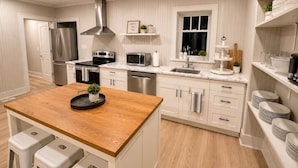 Uma cozinha moderna com armários brancos, eletrodomésticos de aço inoxidável, uma ilha de madeira e uma janela com vista.