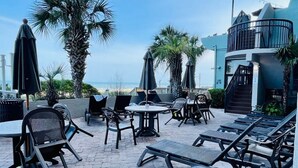 Un patio exterior con sillones, mesas y sombrillas, con vistas a una playa.