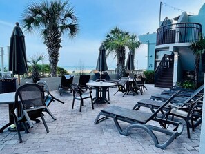 Eine Außenpatio mit Lounge-Möbeln, Tischen und Sonnenschirmen mit Blick auf einen Strand.