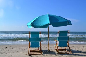 Zwei Liegen mit einem großen Sonnenschirm am Sandstrand.
