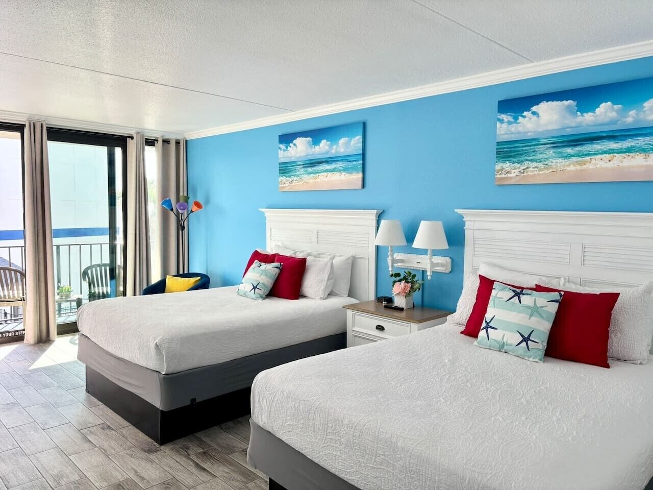A hotel room with two beds, a balcony, and a view of the ocean.
