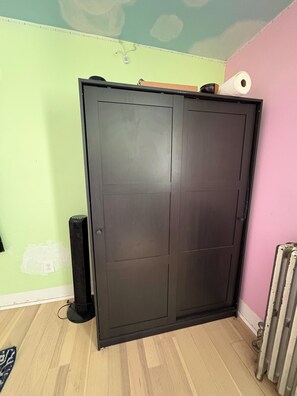 A room with a large wardrobe, a radiator, and a speaker.