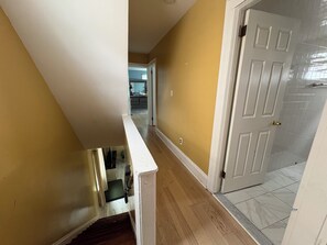 A hallway with a wooden floor, a white door, and a kitchen in the background.