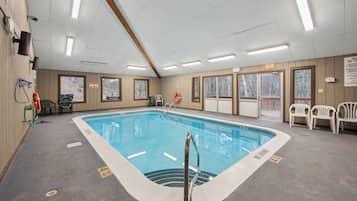 An indoor swimming pool with clear poolside areas, safety equipment, and exit signs.