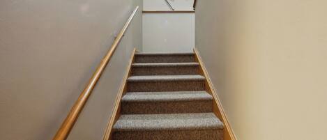 A carpeted staircase with wooden handrails, leading to a landing with a white wall and a ski rack.