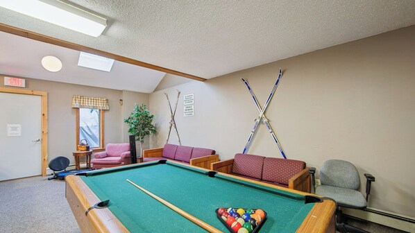 A pool table with a cue stick, a chair, a sofa, and a plant in a room with a door marked 'EXIT'. - Fox Lair by Avantstay Oversized Jetted Tub + Grilling Deck Heated Pool + Recreation Center (North Creek)