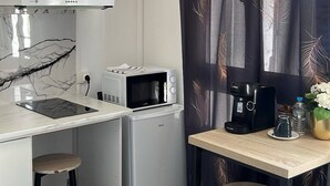 Ett kompakt kök med en mikrovågsugn, brödrost och kaffebryggare på ett litet bord, samt en stol och några pallar.
