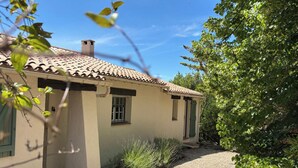 Una casa pequeña con techo de tejas, camino de grava y jardín con diversas plantas.