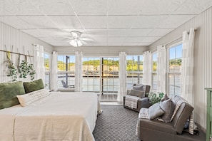 A bedroom with a large bed, a sofa, a ceiling fan, and a view of a water body.