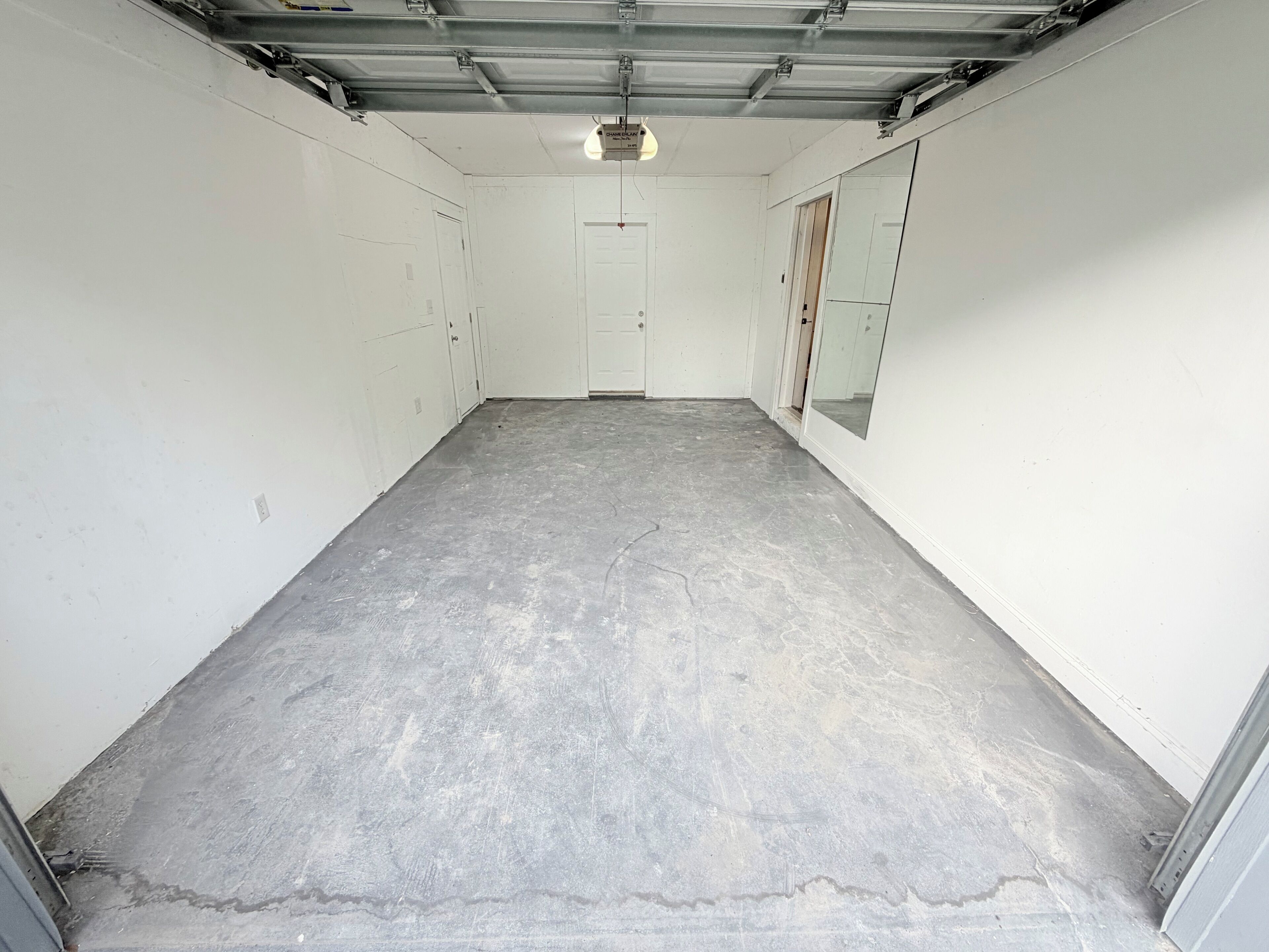 Un garaje con piso de concreto, paredes blancas y una puerta cerrada al fondo.