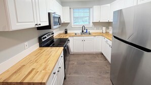 Eine moderne Küche mit weißen Schränken, einem Edelstahl-Kühlschrank, einer Mikrowelle und einer Holz Arbeitsplatte.