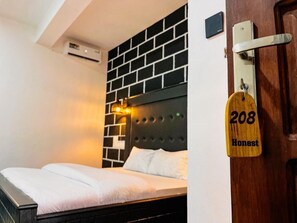 A hotel room with a bed, a black brick wall, a wooden door with a number sign, and an air conditioning unit. - Bamboo Savanna Villas (Arusha)