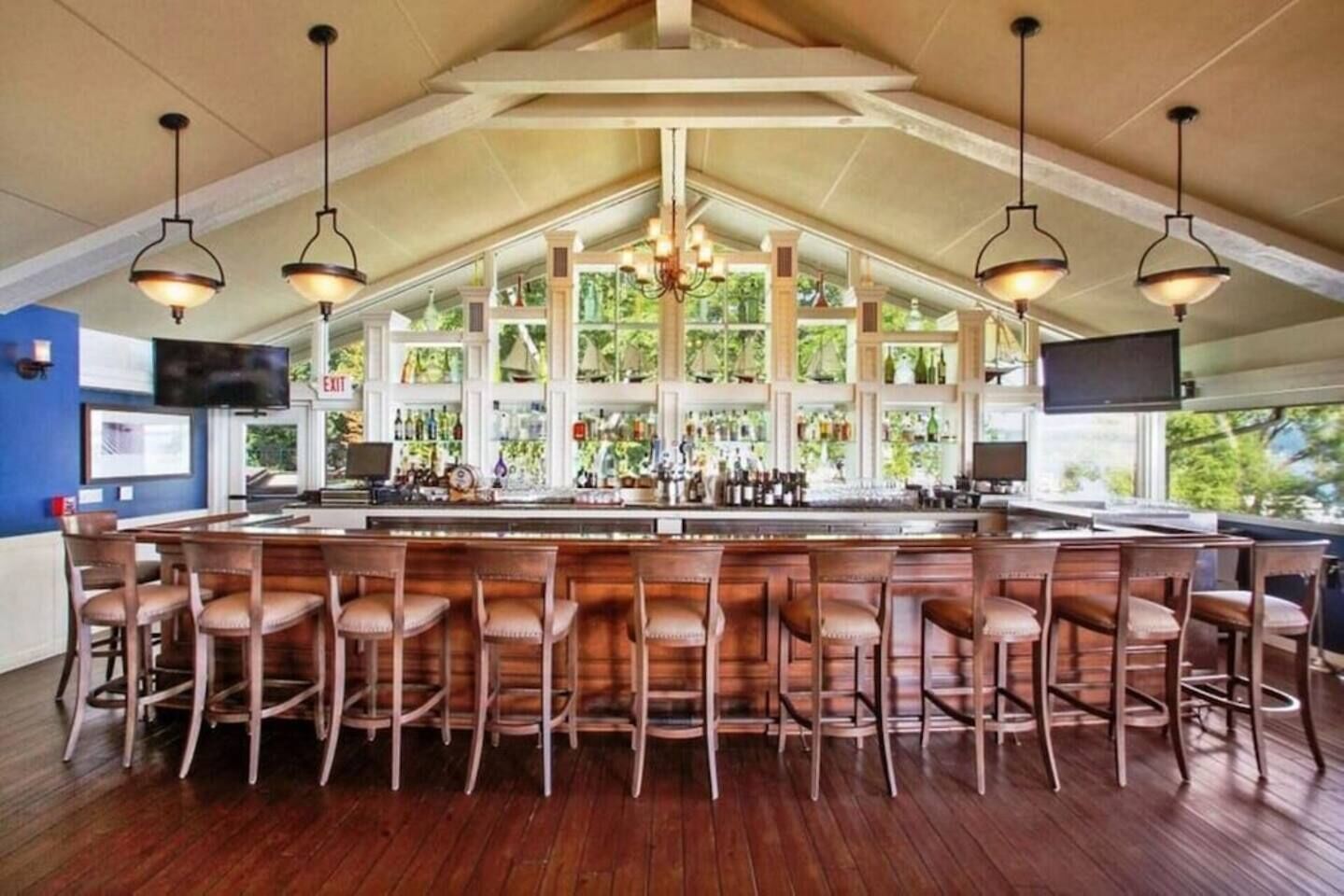Zona de bar con taburetes de madera, techo alto con vigas a la vista y un ventanal con vistas a la vegetación.