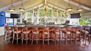 A bar area with wooden bar stools, a high ceiling with exposed beams, and a large window overlooking greenery. - The Perfect Lake Geneva Getaway Awaits (Fontana-On-Geneva Lake)