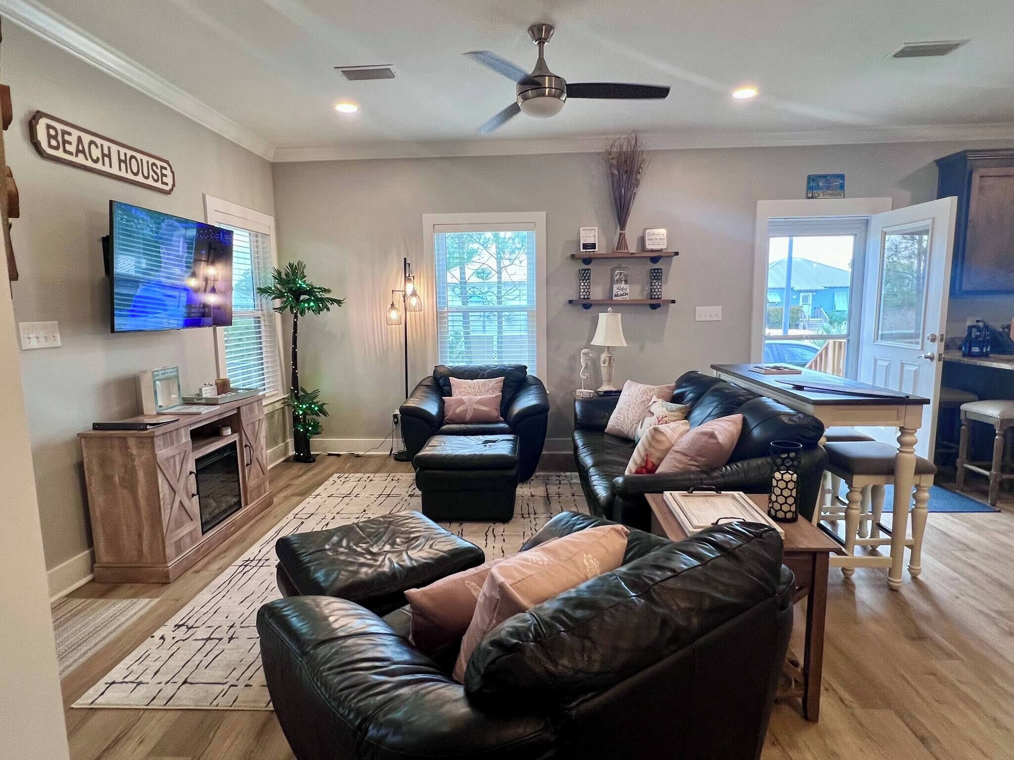Ein Wohnzimmer mit Fernseher, Ledersofas, Deckenventilator und einem Schild mit der Aufschrift 'BEACH HOUSE'.