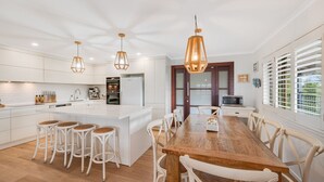 Una cucina moderna con mobili bianchi, un'isola centrale con sgabelli, illuminazione a sospensione e un'area pranzo con tavolo e sedie in legno.