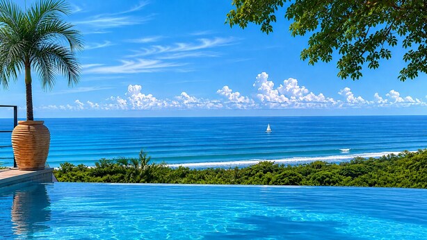 Cel blau clar, mar tranquil·la, un veler i una piscina amb una palmera.