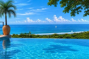 Ein klarer, blauer Himmel, ruhiges Meer, ein Segelboot und ein Pool mit einer Palme.