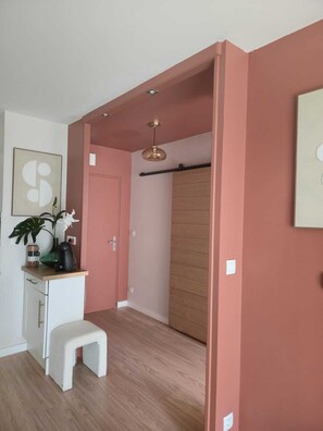 A room with a wooden floor, a white bench, a door, a coat rack, and a hanging light fixture. - A beautiful, cozy apartment (La Chapelle-sur-Erdre)