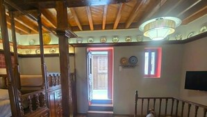 Uma escada de madeira leva a um patamar com um candelabro, uma porta e uma TV na parede.