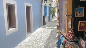 Uma rua estreita com calçada de pedra, edifícios azuis e uma loja que vende bolsas.