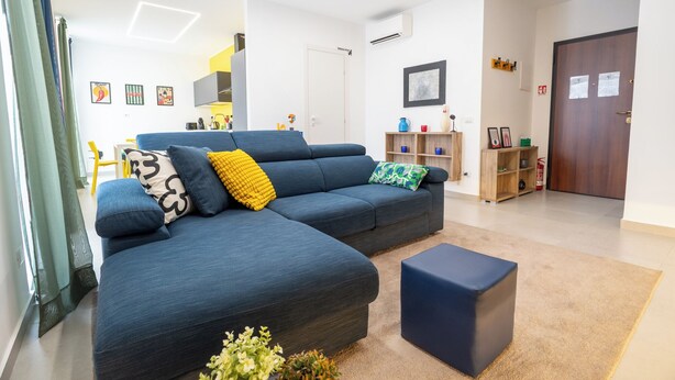 A modern living room with a sectional sofa, a coffee table, and a bookshelf. - Colorama Home - Confort Loft  (Catania)