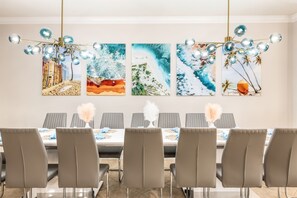 Ein Essbereich mit einem langen Tisch, grauen Stühlen und einer Chandelüster.