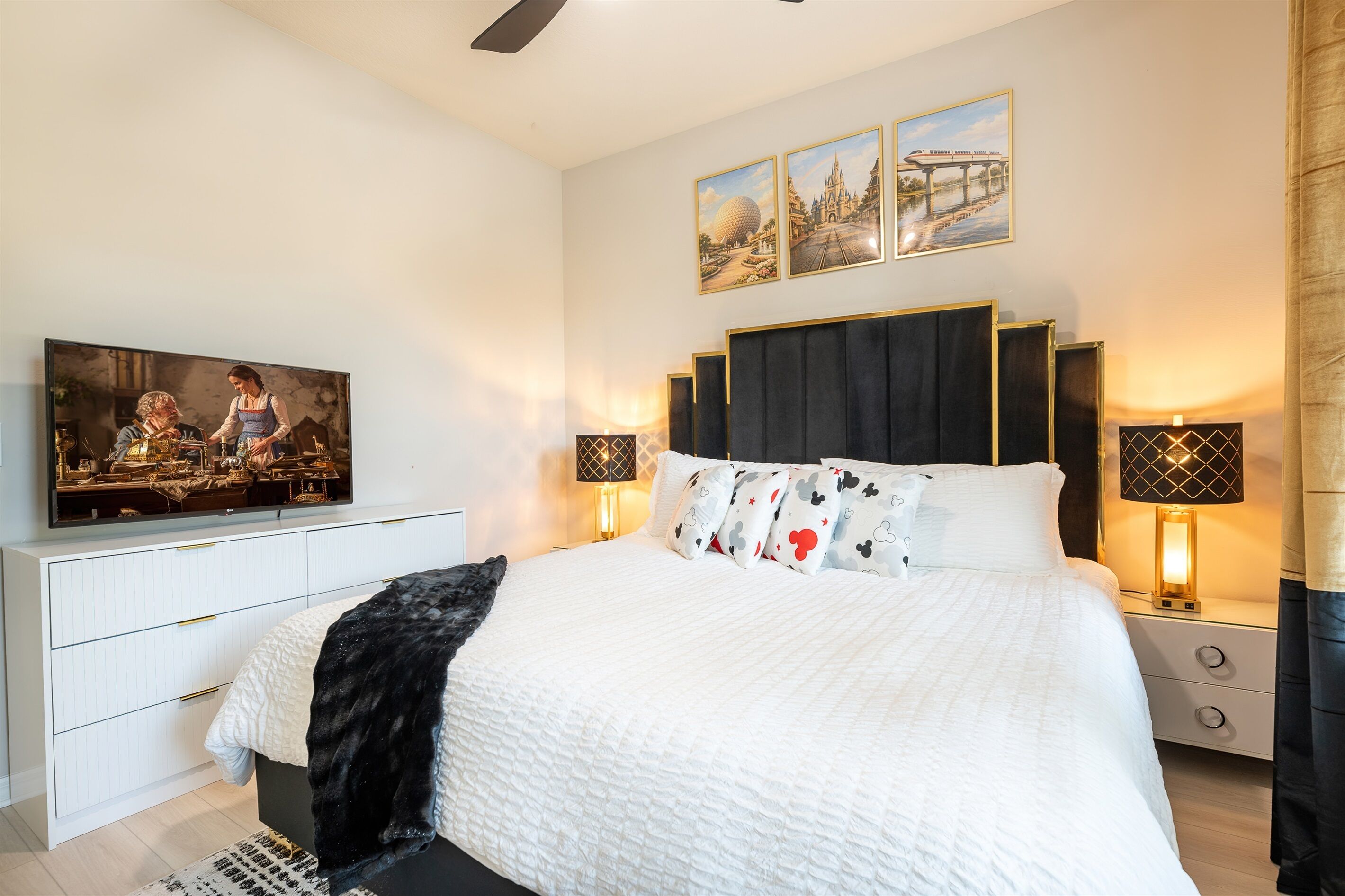 Un dormitorio con cama, televisor, mesita de noche y decoración en la pared.