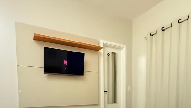 Una habitación de hotel con cama, televisión montada en la pared, puerta y cortina.