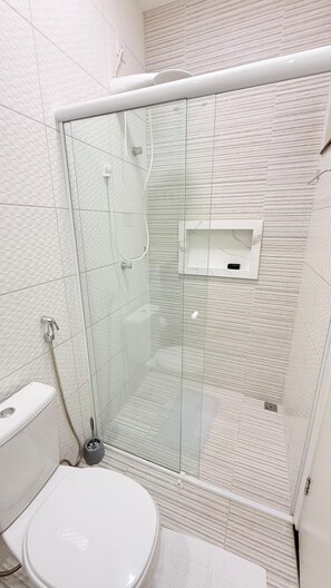 Et moderne badeværelse med brusekabine i glas, toilet og en lille hylde til opbevaring.
