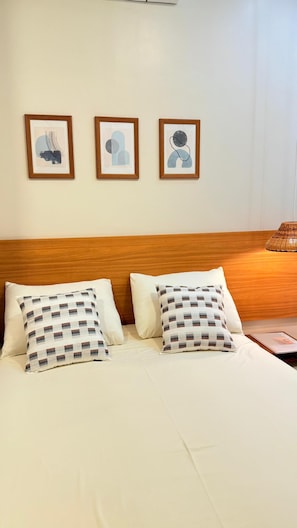 Hotellihuone, jossa on puinen sängynpääty, kaksi sänkyä ruutukuosisilla tyynyillä ja kolme kehystettyä taideteosta seinällä.