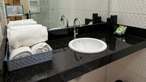Un baño moderno con un lavamanos blanco, encimera negra y un espejo. Hay toallas dobladas en un atril y un cubo de basura negro.