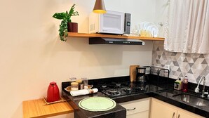 Una cocina moderna con estufa a gas, dos taburetes de madera, microondas y luces colgantes.