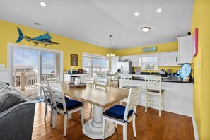 A bright kitchen with white cabinets, a wooden dining table, and a view to the outside. - NEW! Emerald Isle 2nd-Row Luxury 5BR/5+BA Home w/ Pool, Hot Tub & Ocean Views (Emerald Isle)